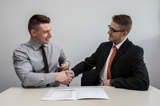 Two men in business attire smiling and shaking hands