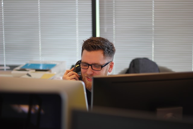 A male employee smiling and talking on the phone in front of a computer