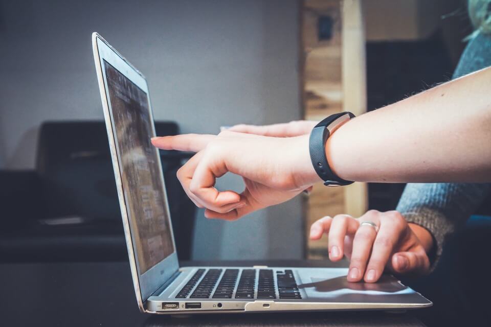Two people pointing to images on a website using a laptop