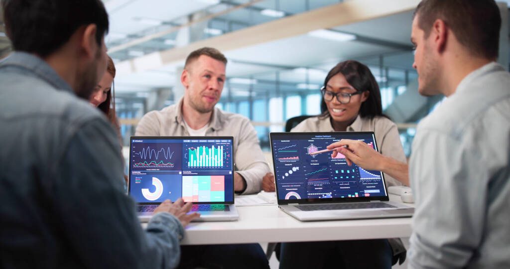 Group meeting with multiple computer screens showing charts and graphs