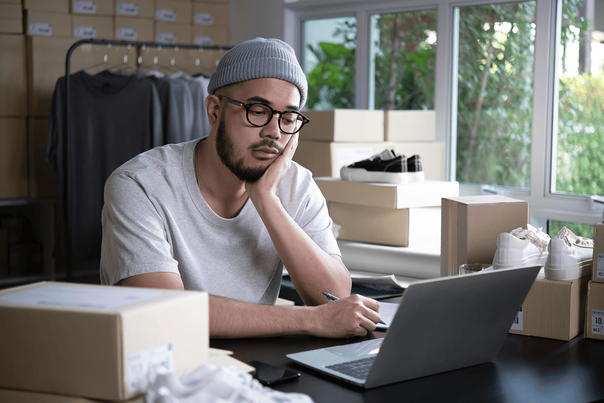 Male in a gray cap with his left hand at his cheek looking at a laptop screen