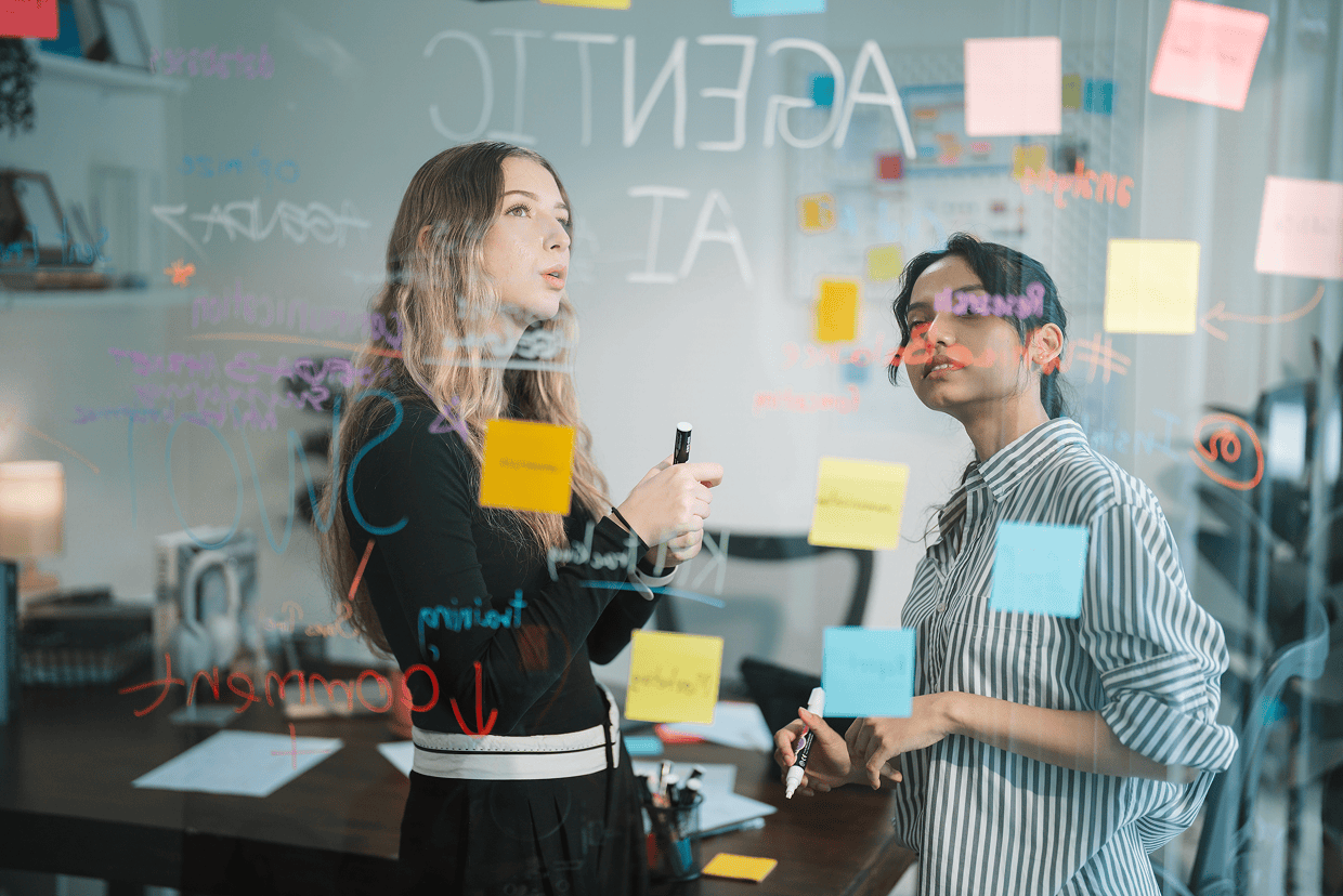 Two females looking at a transparent board with post its and markings